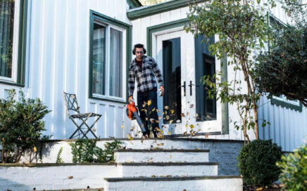hombre con un soplador de hojas en el porche de una casa de campo